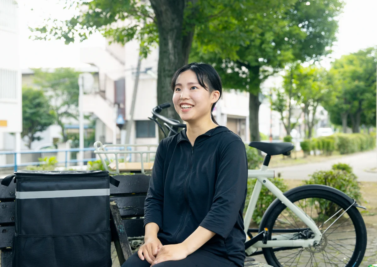 自転車の横で笑顔で話す20代のフードデリバリー配達員のひかりさん